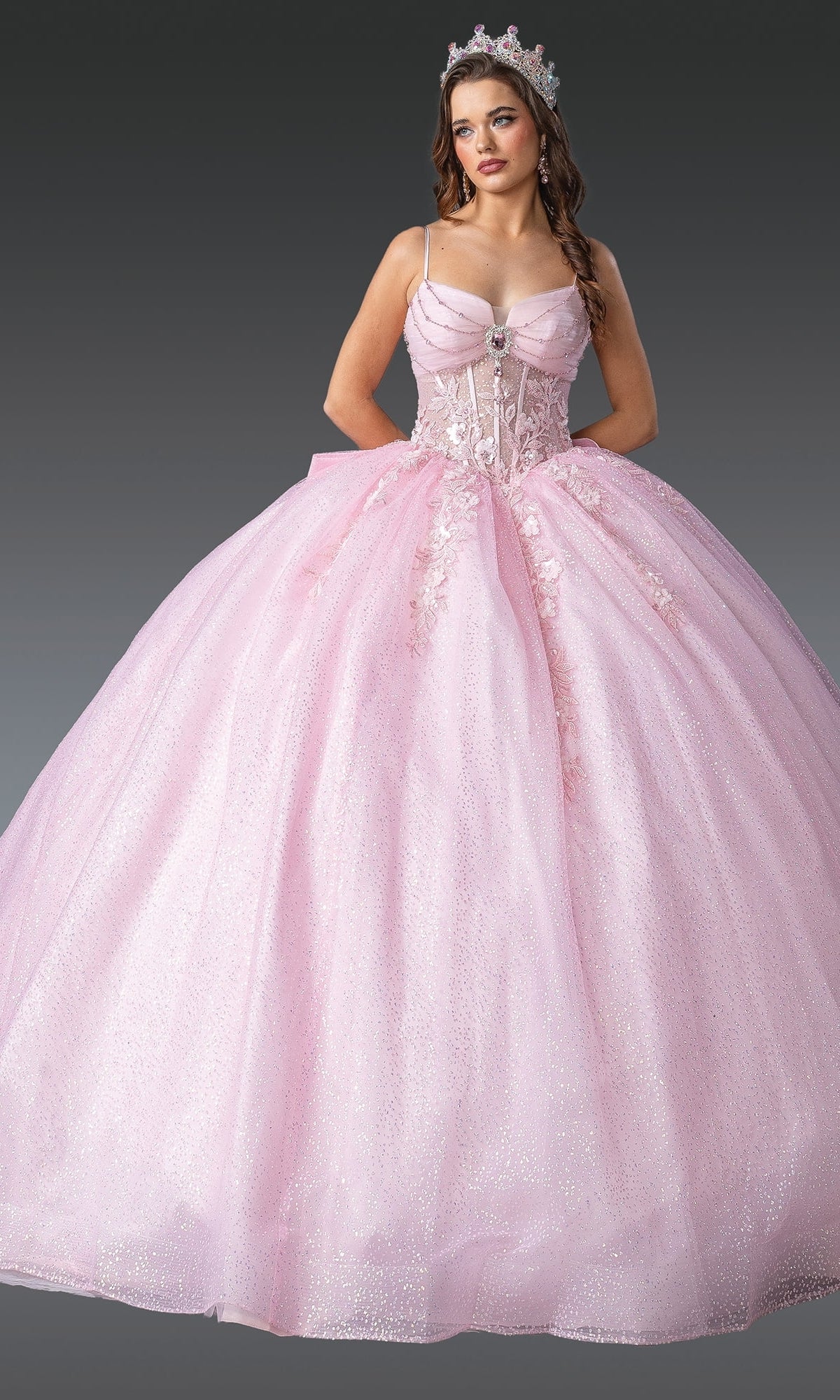 A young woman wears the Dancing Queen 1958 Long Quinceañera Dress with Bow and a tiara, standing against a plain gray background.